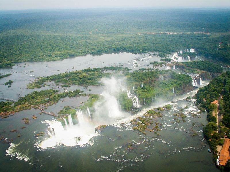 Aerial view of Iguazu Falls surrounded by lush green forest and mist rising from the cascades.
